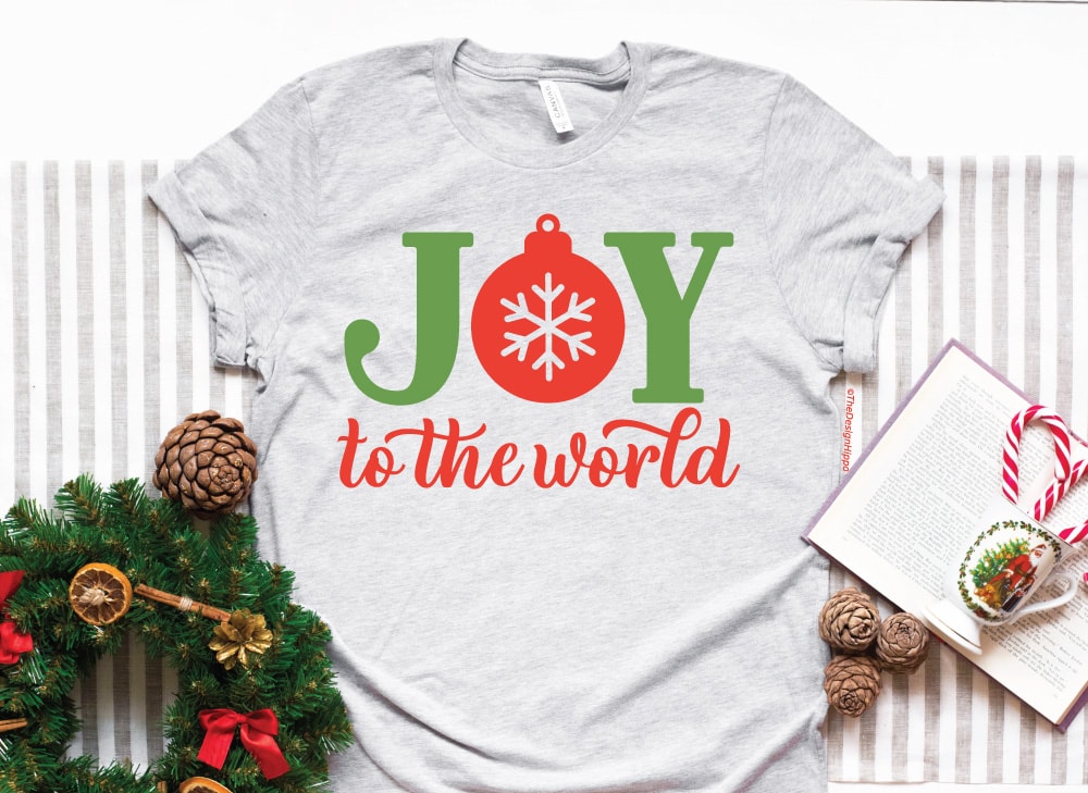 free christmas svg quote, joy to the world with a snowflake and bobble, mocked up on a light grey t-shirt