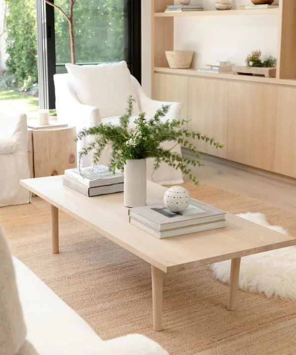 Light wood coffee table with minimal styling featuring books, white ceramic vase, and fresh greenery
