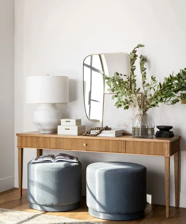 Ribbed wood console table with mirror, gray ottomans, and decorative items in a modern entryway