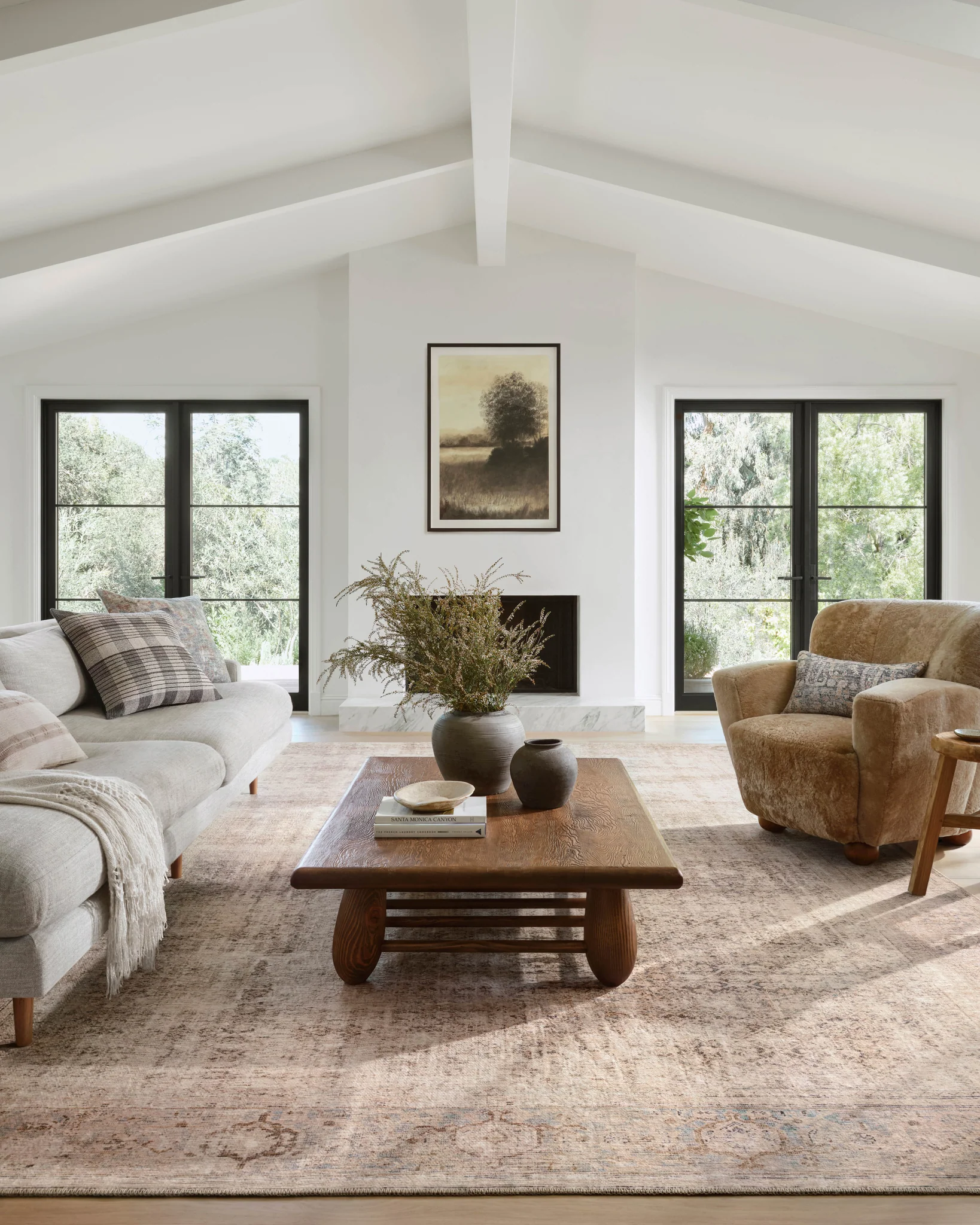 Bright organic modern living room with vaulted ceiling, black-framed windows, wooden beams, and neutral furniture