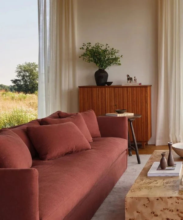 Rust-colored velvet sofa with ribbed wood cabinet and floor-length curtains in modern space