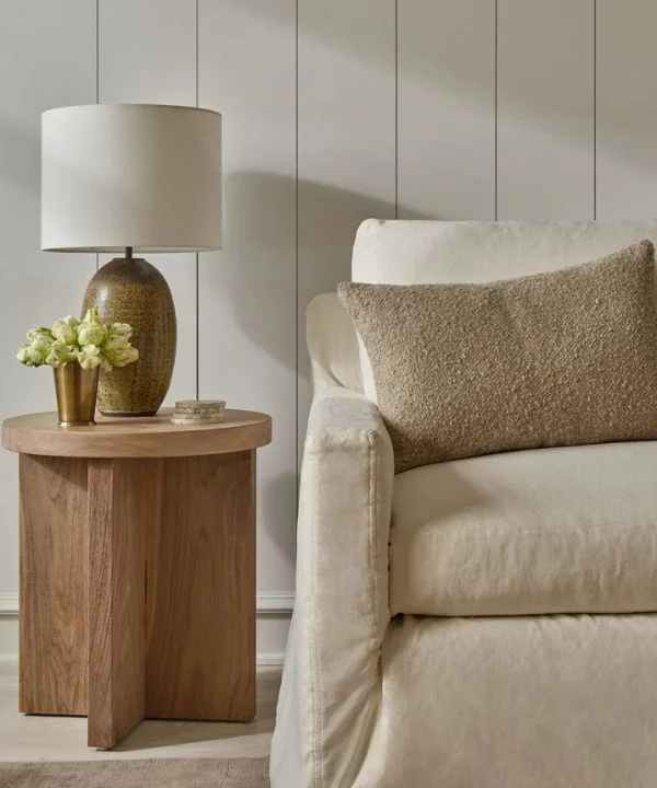 Cross-base wooden side table with ceramic lamp and brass accents in neutral room