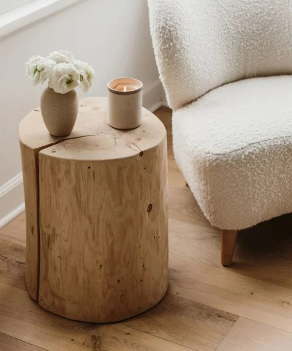Natural wood stump side table next to white bouclé chair with candle styling