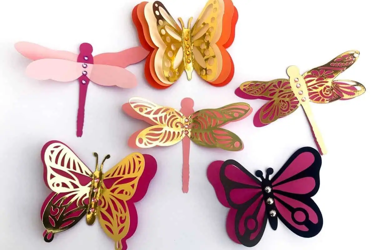 layered paper butterflies and dragonflies in pink, gold and burgundy arranged on a white wall