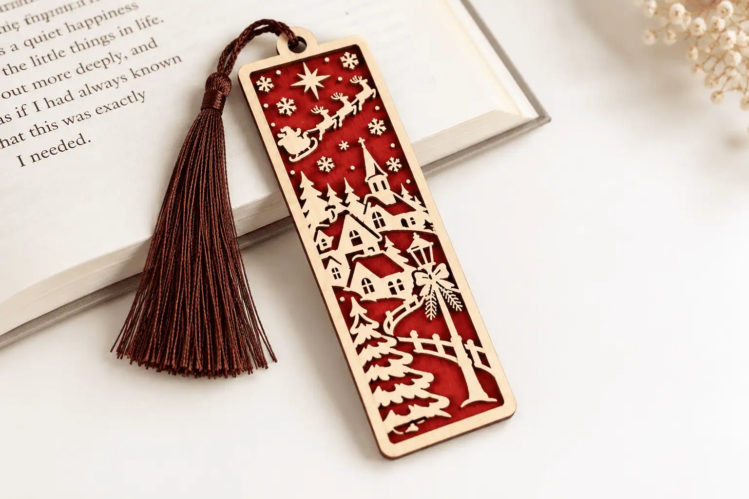 layered Christmas bookmark with a snowy village, trees and a flying sleigh over red, with a red tassel