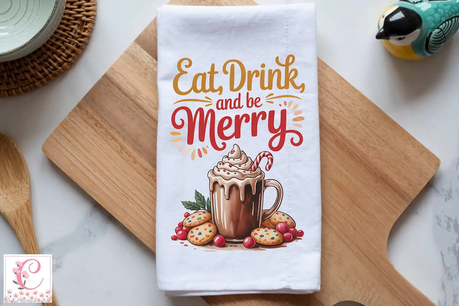 white kitchen towel that says eat drink and be merry with a mug of hot cocoa, whipped cream and cookies