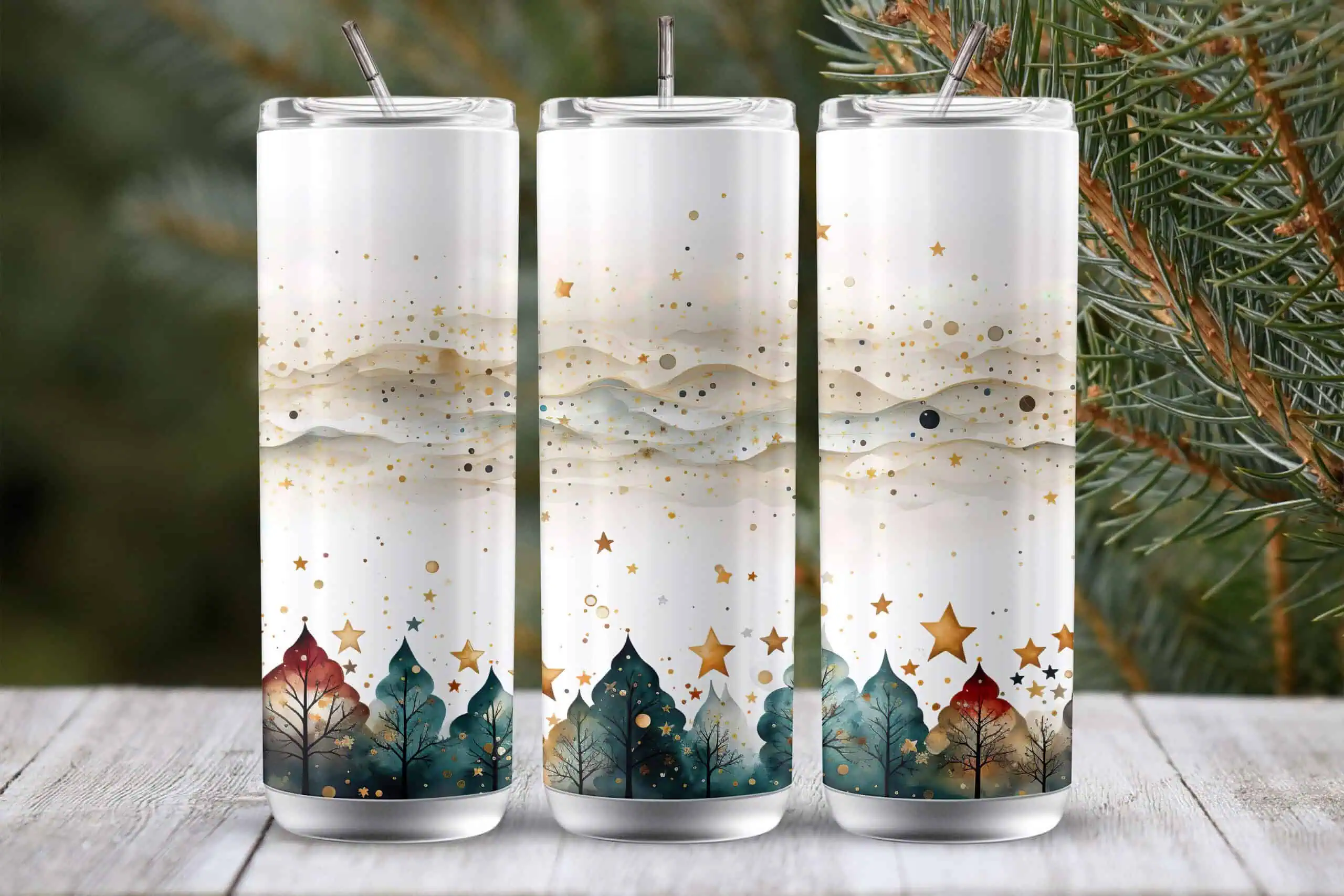 three white skinny tumblers with gold stars, soft snowy hills and a green pine forest along the bottom