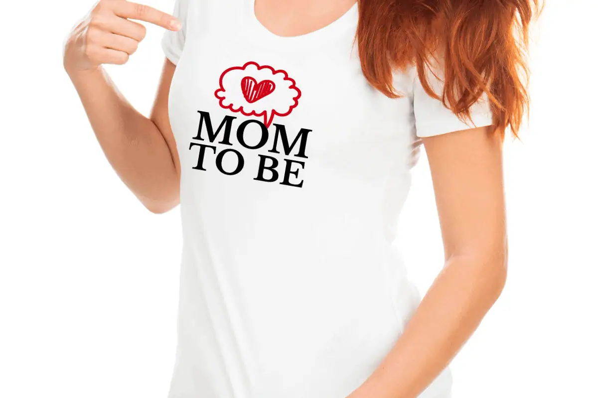 woman wearing a white t-shirt that says mom to be with a red heart in a speech bubble