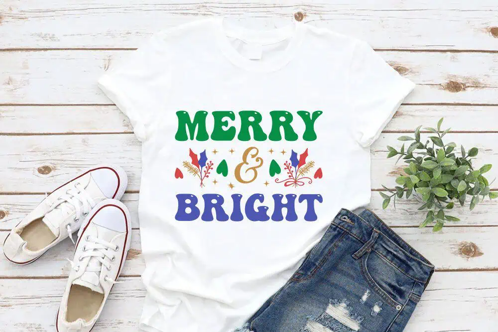 white t-shirt that says Merry and Bright in green and blue retro letters with little holly leaves