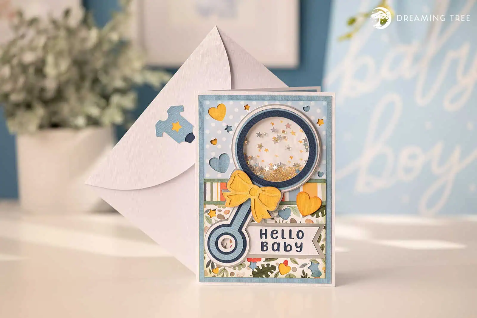 blue baby card with a rattle shaped shaker window full of sequins, a yellow bow and a hello baby label
