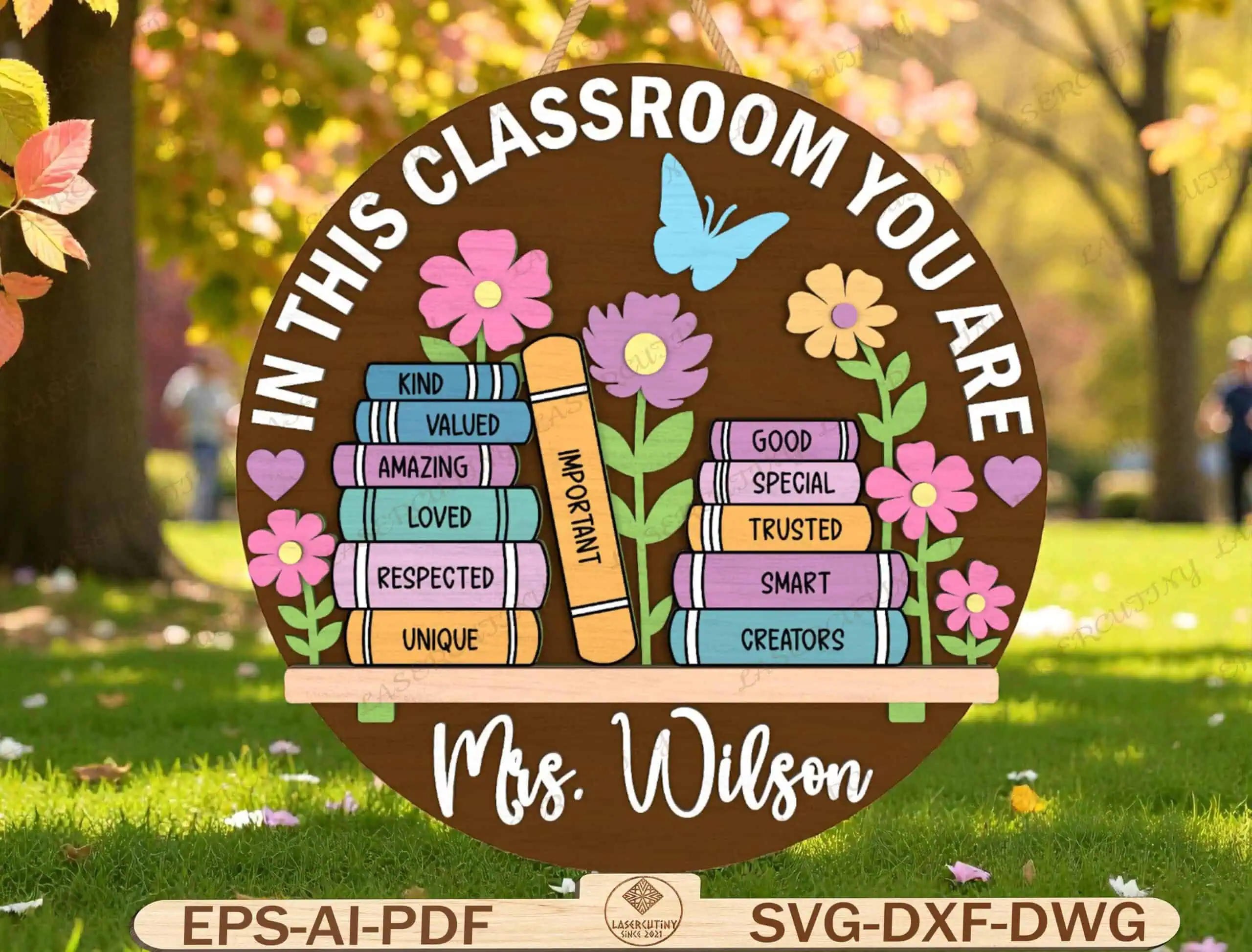 round classroom door sign that says in this classroom you are, with a stack of books labeled kind, valued and loved, flowers and the name Mrs. Wilson