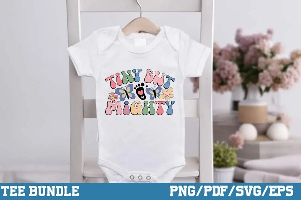 white baby onesie that says tiny but mighty in colorful retro letters hanging on a chair